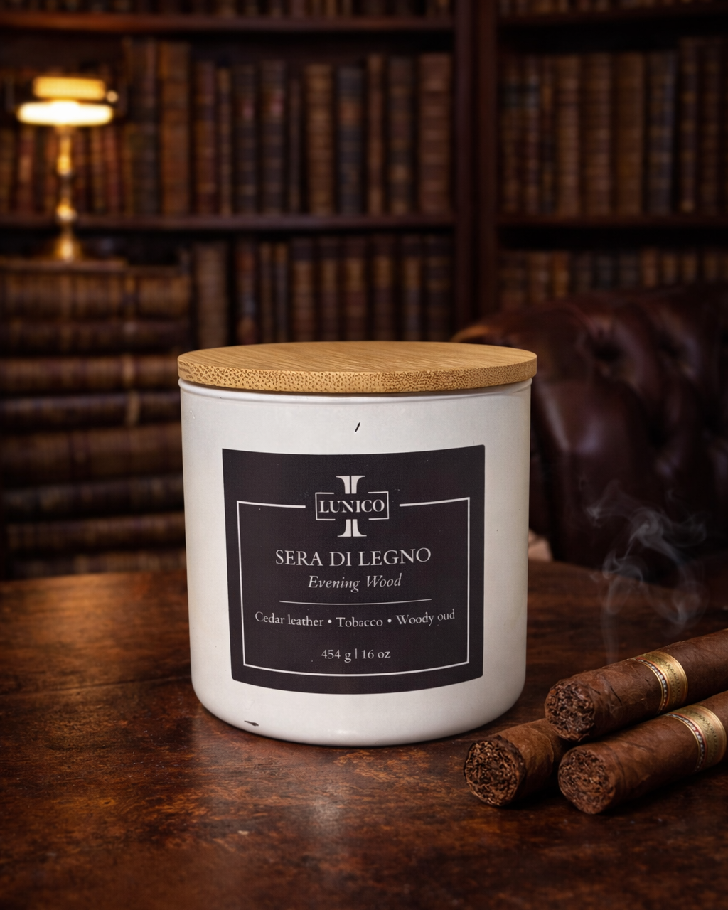 Candle labeled 'Sera di Legno' on a wooden surface with cigars and a bookshelf in the background